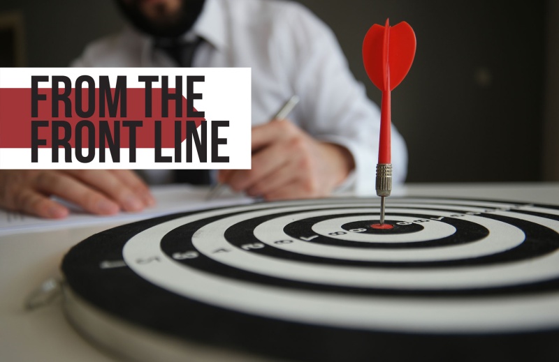 A businessman in a suit taking notes behind a dartboard with a bullseye, symbolizing strategic planning and success in the insurance industry, highlighting Smart Choice and Express Markets' business growth despite a hard market.