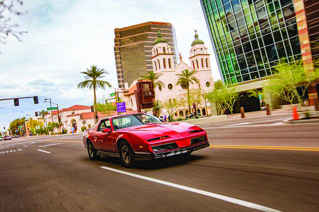 A red classic sports car drives down a four lane road.