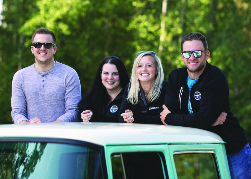 A group of Millennials lean on the roof of a collector car.
