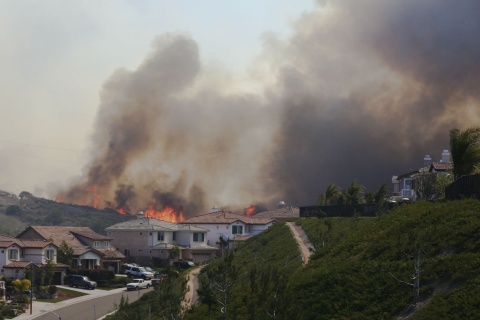 A neighborhood on a hillside with wildfires burning in the background.